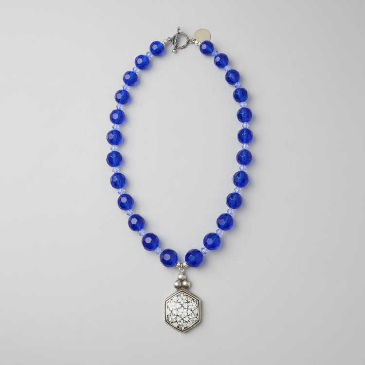 Brilliant cobalt blue takes center stage in this one-of-a-kind handcrafted Billielephante necklace. Rich, transparent faceted blue glass beads are individually separated by petite iridescent crystal-style spacers, creating exceptional sparkle as the necklace catches the light.

The strand leads to an oversized silver-tone geometric statement pendant, featuring an intricate mosaic-like reflective center and dimensional metal border. Decorative silver-tone hardware completes the eclectic artisan design.

Bold