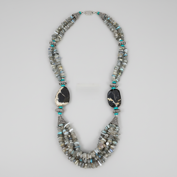A striking one-of-a-kind handcrafted statement necklace from the Billielephante Jewelry Collection, featuring layers of natural Labradorite chips with their characteristic gray tones and subtle flashes of blue and green.

The necklace is accented with vibrant Turquoise beads, ornate German silver-tone components, and dramatic faceted Tiger Agate stones. Multiple strands of irregular Labradorite create wonderful texture and movement, while the oversized dark stones and detailed silver-tone spacers give the p