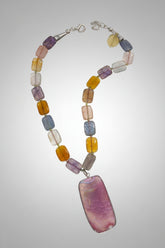 A collection of smooth rectangular agate-style stone beads travels around the necklace in shades of lavender, smoky blue-gray, translucent blush, honey amber and golden yellow. Each bead displays its own variations in color and pattern, creating the collected, globally inspired character that defines the Billielephante collection.
